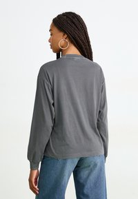 Chemise grise à manches longues avec une coupe décontractée, un col rond et des poignets côtelés. Associée à un jean bleu taille haute. Tissu en coton doux.