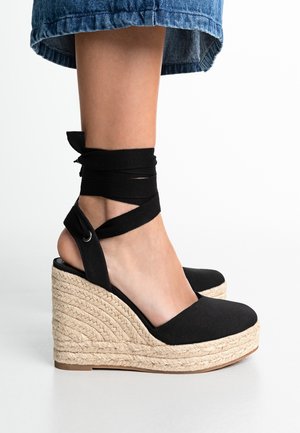 Czarne sandały na koturnie z płóciennym sznurkiem, z plecioną jucie platformą i wiązaniami na kostce, z zaokrąglonym noskiem i otwartym designem pięty.