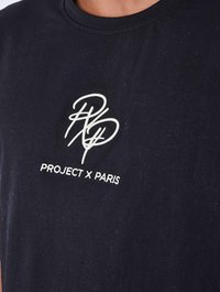 Camiseta de algodón negra con logo y texto bordado en blanco "PROJECT X PARIS" en el pecho, diseño de cuello redondo y textura suave.