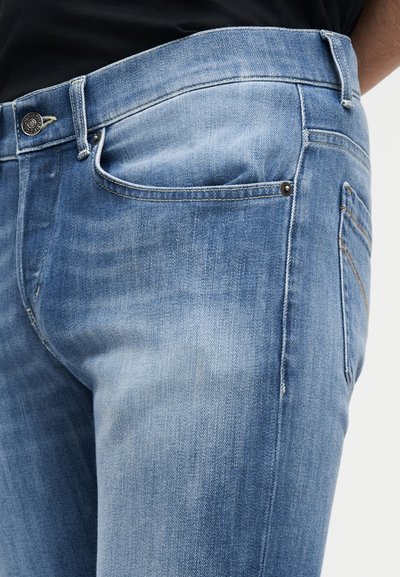 Κοντινό πλάνο ανοιχτόχρωμων τζιν denim που φοριούνται με μαύρο πουκάμισο, δείχνοντας τις μπροστινές και πλαϊνές τσέπες καθώς και τις μεταλλικές λεπτομέρειες με καρφάκια.