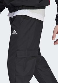 Pantaloni cargo neri in tessuto testurizzato, con il logo Adidas bianco sulla parte superiore della gamba sinistra e tasche laterali per il ripostiglio.
