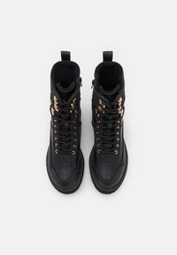 Botas altas negras de cuero, con un diseño de cordones y ojales en tono dorado, y un forro texturizado. Cierre de cremallera en el lateral.