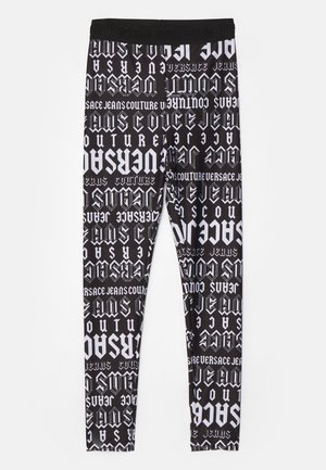 Sorte tights med et gjentakende hvitt grafisk mønster av ulike stiliserte tekster, inkludert "Versace Jeans Couture", og en solid midjebånd.