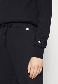 Svart sweatshirt och byxor med broderad logotyp. Mjuk tyg med ribbad midja och ärmslut, dragsko-detalj på byxorna.