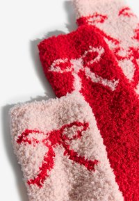 Calcetines de felpa en rojo y rosa claro con un diseño de lazo. Textura suave con un acabado de felpa; detalles rojos sobre el fondo rosa claro.
