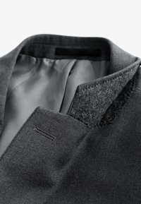 Col et revers de blazer gris avec coutures visibles et doublure intérieure lisse, montrés en gros plan.