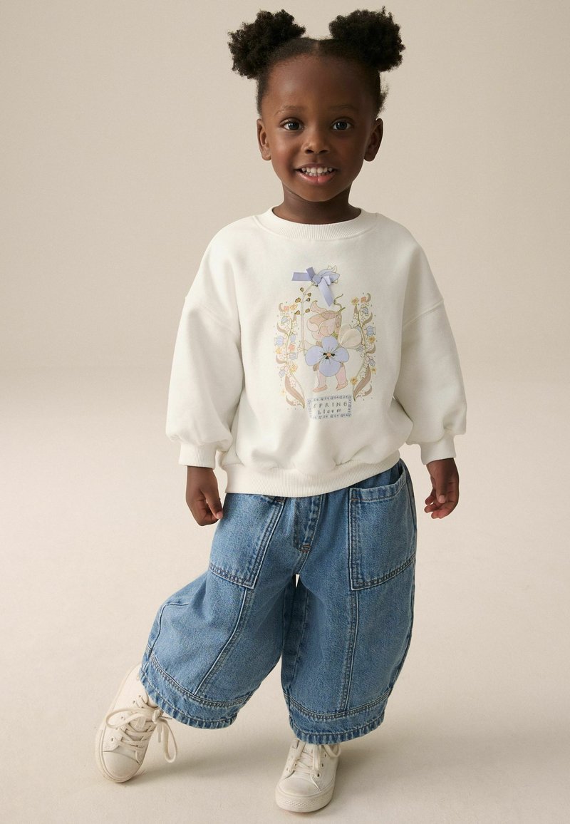 Weißer Sweatshirt mit floralen Grafiken und Schleifendetails, kombiniert mit weiten blauen Jeans und weißen Sneakers. Einfaches und bequemes Design.