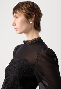 Zwarte blouse van doorschijnende stof met kantdetails. Heeft een hoge halslijn met kant afwerking en pofmouwen voor een gestructureerde uitstraling.