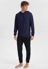 Marinblå hoodie med dragsko, ribbade ärmslut och avslappnad passform, ihop med svarta jogger-byxor med elastiska manschetter och sidofickor.