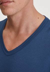 Marineblauwe V-hals t-shirt met een zachte, gladde textuur en fijne stiksels rond de halslijn, waarbij de gedeeltelijke nek en kaaklijn van een persoon zichtbaar zijn.