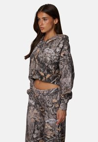 Geknipte camouflage hoodie en bijpassende sweatpants in bruin en groen, met bladpatronen en geborduurde logo-details op beide stukken.