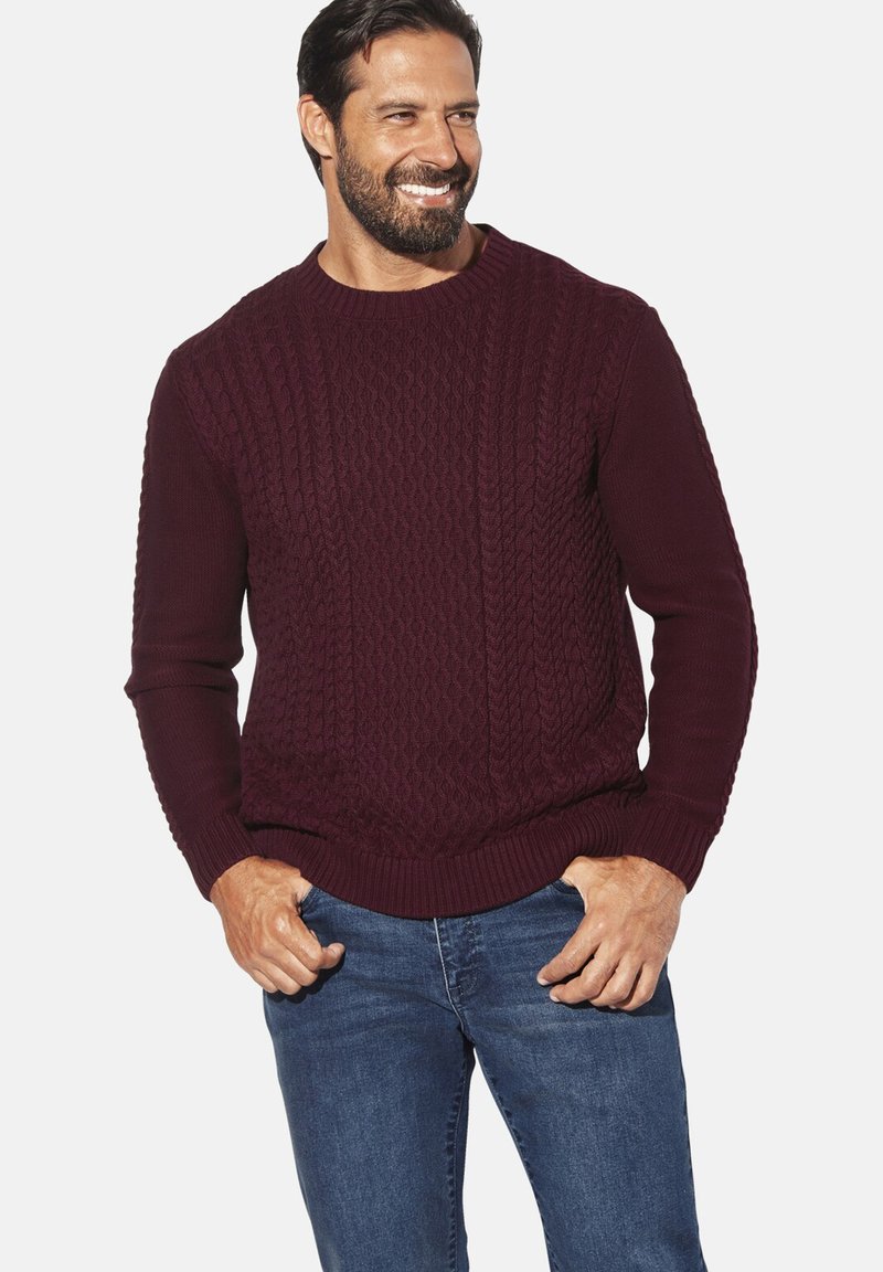 Bordeauxroter Strickpullover mit strukturiertem Zopfmuster, gerippten Bündchen und Saum. Kombiniert mit blauer Jeans.