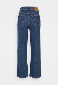 Jean en denim bleu à jambe droite vu de dos avec deux poches cousues et un patch en cuir marron de marque à la taille.