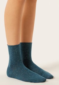 Morskie zielone skarpetki załogowe wykonane z miękkiego, teksturowanego materiału o delikatnym połysku, z żebrowanym mankietem i nakrapianym wzorem na całej powierzchni.