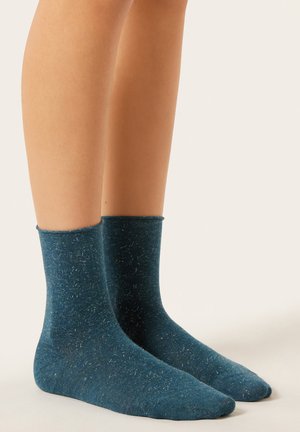 Grüne Crew-Socken aus weichem, strukturiertem Stoff mit leichtem Glanz, versehen mit einem gerippten Bündchen und einem durchgehenden gesprenkelten Muster.