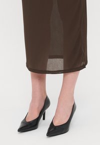 Melni ādas augstpapēžu apavi ar norādītu pirkstu dizainu, ar gludu tekstūru un šauru papēdi, uz neitrāla fona.