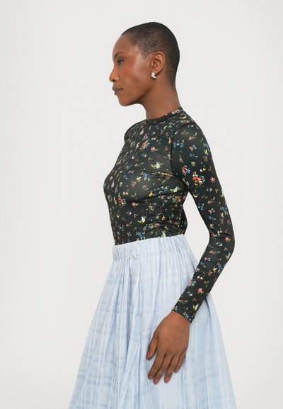 Bluză neagră cu mânecă lungă și model floral, asociată cu o fustă bleu deschisă, plisată. Materialul pare neted și are un design ajustat.