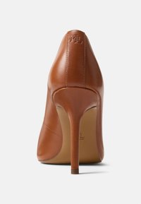 Καφέ δερμάτινη γόβα με ψηλό τακούνι και μυτερή μύτη, κομψού σχεδιασμού. Διαθέτει λεπτό τακούνι και ανάγλυφο λογότυπο στο πίσω μέρος.