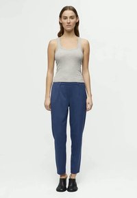Grijze tanktop, blauwe op maat gemaakte broeken met zijzakken en zwarte instappers. Eenvoudig ontwerp, soepele textuur, aangesloten pasvorm.