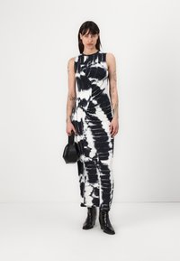 Rochie maxi tie-dye alb-negru, cu un design mulat, fără mâneci, cu strângere pe lateral și o cădere fluidă a materialului. Asortată cu pantofi cu toc negri.
