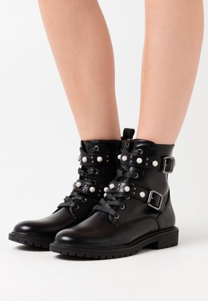 Botas de tobillo de cuero negro con hebillas decorativas, acentos de perlas y cordones. Suela de goma texturizada para tracción y durabilidad.