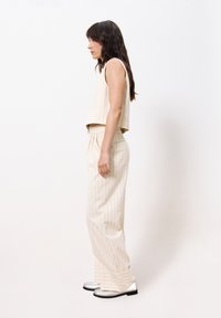 Beige gestreifter Crop-Top mit einem kastenförmigen Design, kombiniert mit hoch taillierten, schmal zulaufenden Hosen und metallisch silbernen Schuhen. Glatte Stoffstruktur.