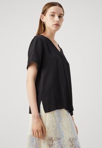 Top negru cu decolteu în V și mâneci scurte, având o margine decorativă la tiv, asortat cu o fustă ușoară din dantelă. Material moale cu o croială lejeră.