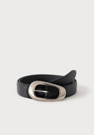 Ceinture en cuir noir texturé avec une boucle argentée brillante de forme ovale irrégulière, enroulée sur un fond uni gris clair.