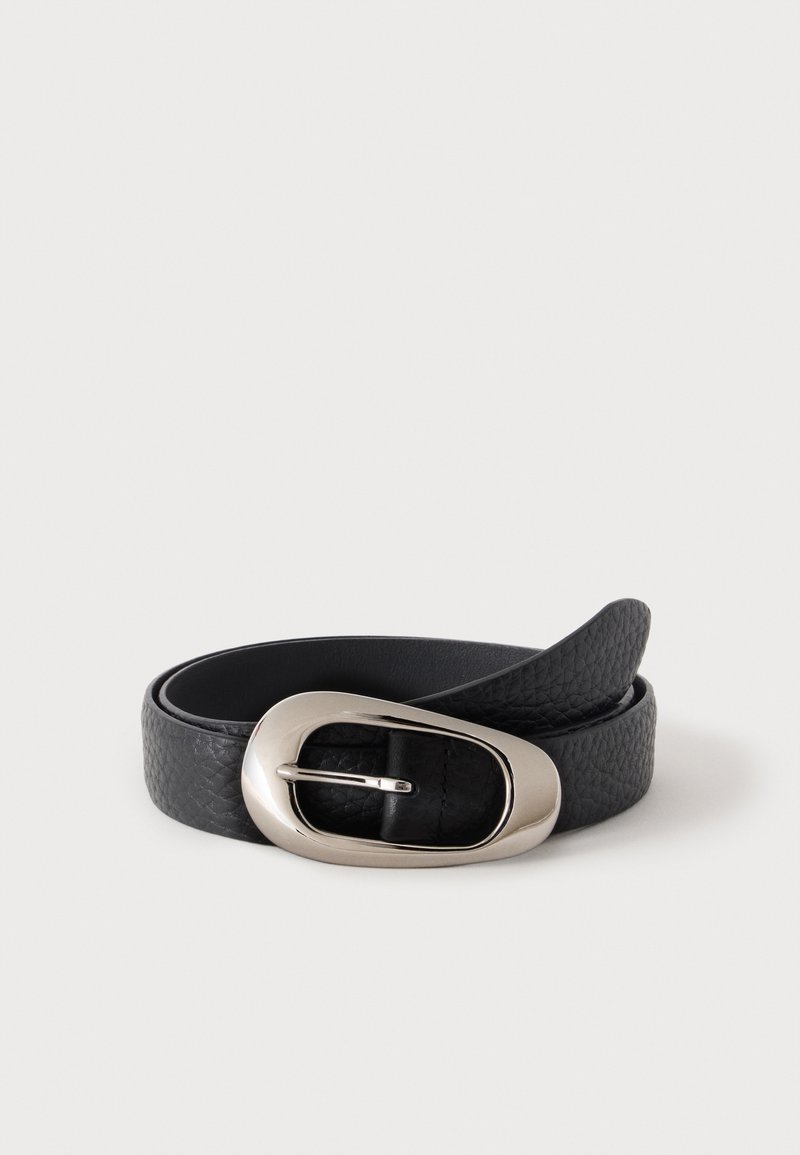 Ceinture en cuir noir texturé avec une boucle argentée brillante de forme ovale irrégulière, enroulée sur un fond uni gris clair.