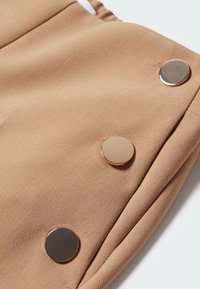 Tissu beige avec trois grands boutons métalliques ronds et brillants disposés verticalement près d'un bord plié.