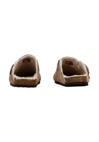 Chaussures à enfiler en suede marron avec une doublure blanche moelleuse et une semelle en liège texturée. L'arrière a une forme arrondie et des accents marron contrastants.
