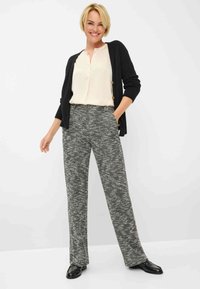 Zwarte cardigan over een crèmekleurige blouse met knopen, gecombineerd met grijze textureerde wijdpijpenbroeken. Model draagt zwarte schoenen en staat voor een neutrale achtergrond.