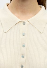 Cremefarvet ribstrikket polo-top med krave, der har fem lyseblå knapper foran, lavet af et tekstureret stof og med en blød, struktureret krave.