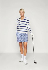 Mėlynos ir baltos dryžuotos megztinio su V formos kaklu, derinamos su gėli�ų rašto mėlyna sijonu. Modelis laiko golfo lazdelę, vilkintis baltus sportinius batelius ir kojines.