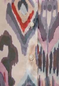 Button-up shirt in lightweight, colorful fabric featuring a bold ikat pattern. Key colors include pink, red, teal, and gray. Two buttons visible.
