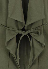 Olivgrön jacka med mjuk textur, med draperad front, öppen krage och knytbar midja för justerbar passform.