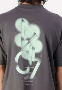 Camiseta de algodón gris con un gran diseño gráfico en verde menta que presenta formas geométricas y texto en la parte posterior. Mangas cortas, corte clásico.