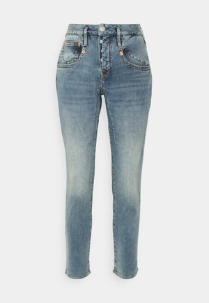 Jean skinny bleu clair taille haute avec braguette à boutons, poches avant, et détails subtilement délavés sur les cuisses et les genoux.
