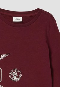Bordeaux lange mouwen shirt met een ronde hals, met witte geprinte graphics van een driehoek en een dinosaurus met tekstaccenten. Zachte textuur.