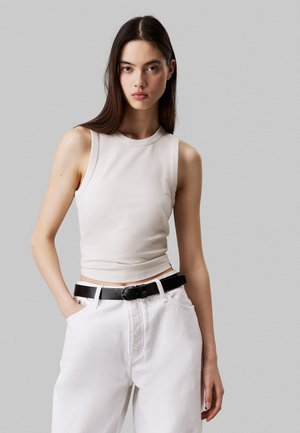Haut sans manches, de couleur beige clair avec un design ajusté. Fabriqué à partir d'un tissu lisse, il présente un col rond et une taille subtile. Associé avec un pantalon blanc.