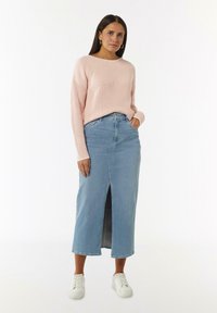 Light pink ribbed sweater, high round neck, paired with a light blue denim maxi skirt featuring a front slit. White sneakers.