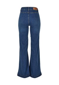 Jean bleu foncé à jambes larges vu de dos avec un patch en cuir de marque sur la ceinture et des coutures visibles.