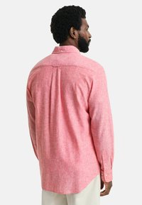 Roze gemêleerde button-up shirt met een rugpand, lange mouwen en een gebogen zoom, gemaakt van lichtgewicht stof. Heeft knoopmanchetten en plooidetail.