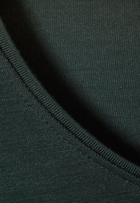Dark green fabric with a smooth texture, showcasing a close-up of the neckline's ribbed trim and fine weave pattern.