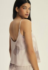 Beżowa bluzka bez rękawów o luźnym kroju, z kwiatowym wzorem w ciemniejszych odcieniach. Materiał jest gładki i błyszczący, z cienkimi ramiączkami.