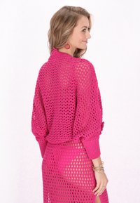 Maglione rosa all'uncinetto con vestibilità ampia e maniche lunghe, abbinato a una gonna coordinata che presenta un motivo a rete aperta e un dettaglio con spacco laterale.
