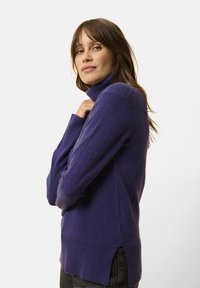 Fialový rolák vyrobený z měkkého materiálu, s žebrovanými manžetami a bočními rozparky na lemu. Jednoduchý, přiléhavý design.