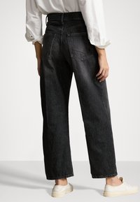 Vaqueros de mezclilla negros de tiro alto, corte recto, con dos bolsillos traseros, textura suave. Combinados con zapatillas de color claro.