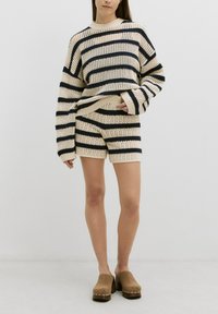 Set in maglia color crema composto da un maglione a strisce e pantaloni corti coordinati. Il maglione presenta ampie strisce di colore blu navy, polsini a coste e un collo rotondo.