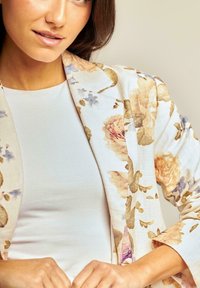 Blazer à motifs floraux en tissu léger aux couleurs pastel et à la coupe décontractée, superposé à un haut blanc uni.